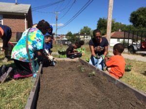 a group of residents gather around a raised bed to plant a community garden and probably then hire a freelance writer